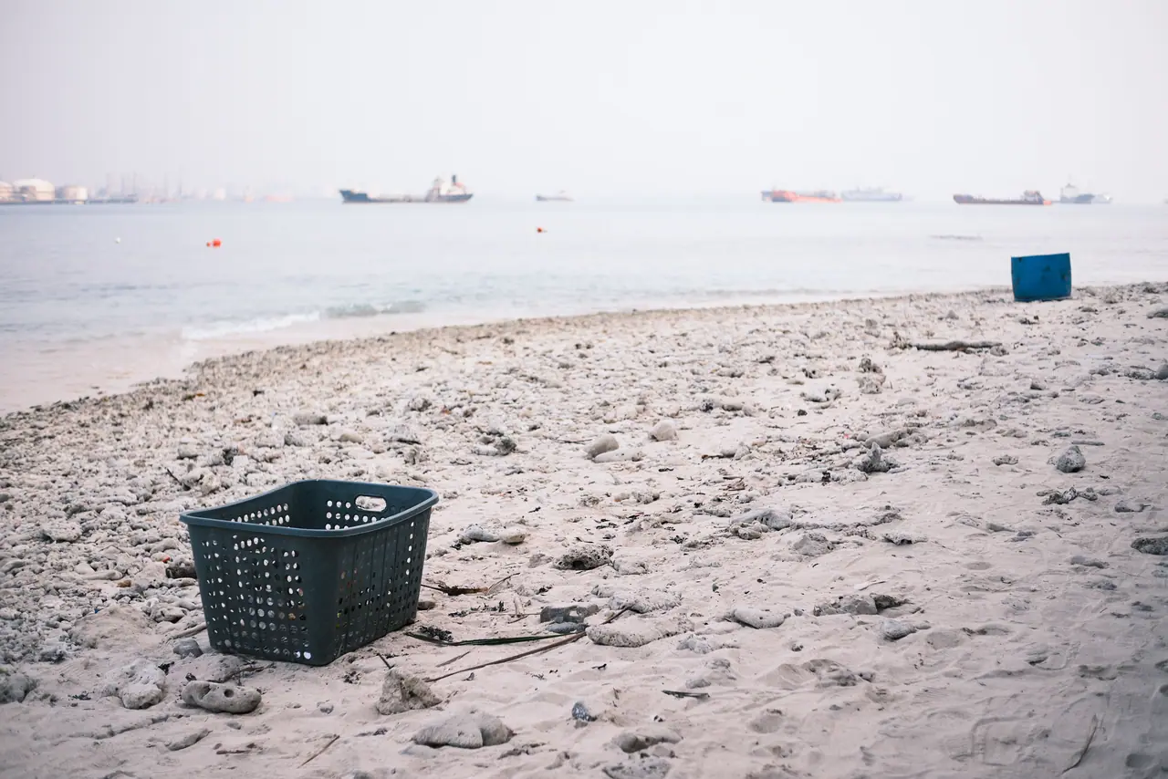 A dark plastic basket on an empty beach with ships on the horizon.