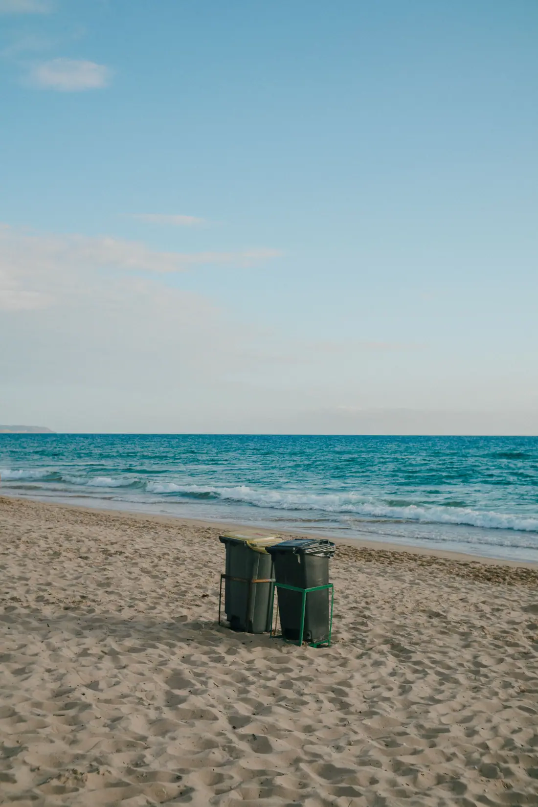 Two waste bins on a sandy beach with waves breaking behind them.